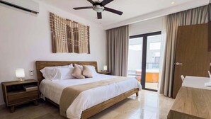 A hotel room with a bed, a nightstand, a ceiling fan, a large window with curtains, and a door. - Luxury Condo: Rooftop Pool, Jacuzzi & Game Room (Playa del Carmen)