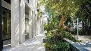 A modern building with a covered walkway, greenery, and a tree. - Luxury Condo: Rooftop Pool, Jacuzzi & Game Room (Playa del Carmen)