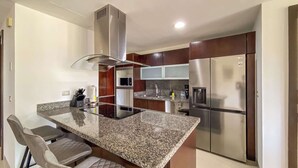 A modern kitchen with a central island, stainless steel appliances, and a built-in microwave. - 2BR Beachfront Condo Playa | Pool & Beach (Playa del Carmen)