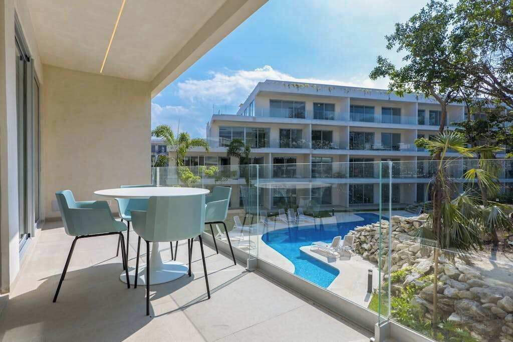 A balcony with a glass railing overlooking a swimming pool and a building with multiple floors.
