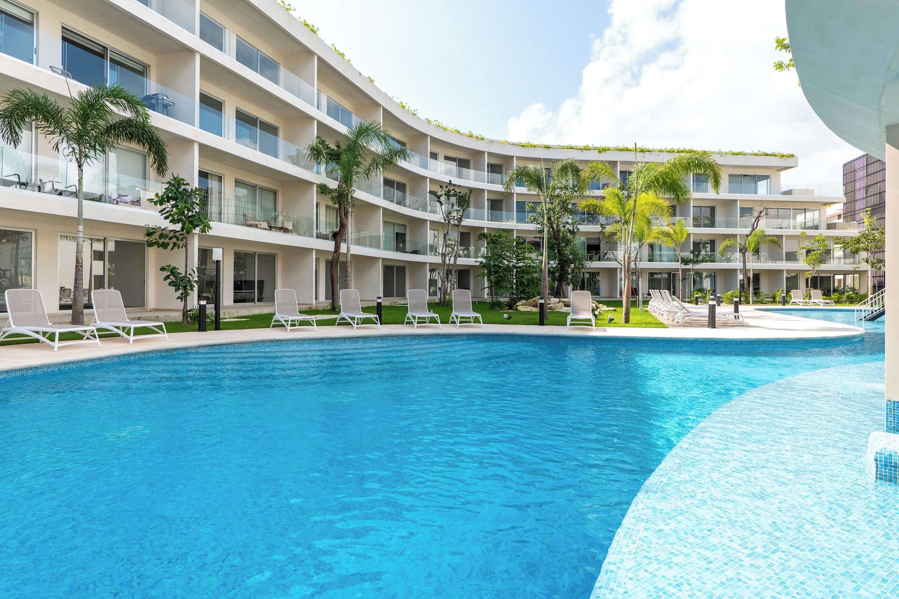 A hotel with a swimming pool, multiple balconies, and palm trees.