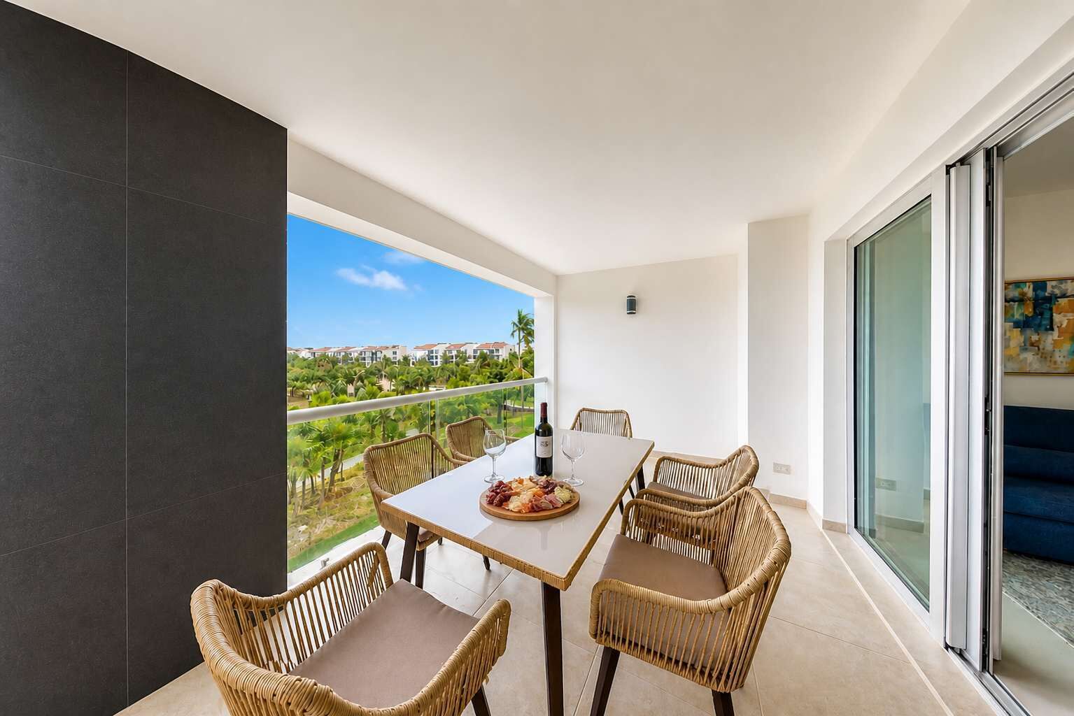 A balcony with a dining table, wicker chairs, and a scenic view of a resort.