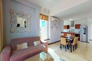 Ein Wohnzimmer mit einer Couch, einem Esstisch mit Stühlen, einer Küche im Hintergrund und einem großen Wandspiegel.