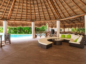 A covered outdoor lounge area with a pool, wicker furniture, and a thatched roof. - Playa del Carmen 3BR Villa | Pool, Gym & Balcony (Playa del Carmen)