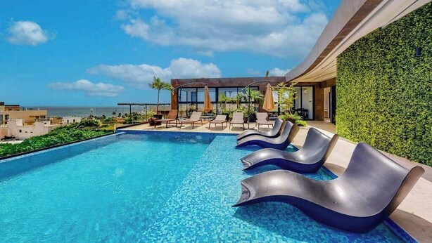 A modern pool area with lounge chairs, a view of the ocean, and a green wall. - Perfect Place 211 | Studio, Rooftop Pool & Gym (Playa del Carmen)