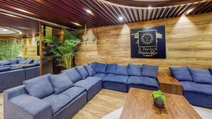 A modern lounge area with a sectional sofa, a wooden coffee table, and a logo on the wall. - Perfect Place 211 | Studio, Rooftop Pool & Gym (Playa del Carmen)