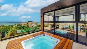 A modern building with a large glass window, a wooden deck, and a hot tub. - Perfect Place 211 | Studio, Rooftop Pool & Gym (Playa del Carmen)