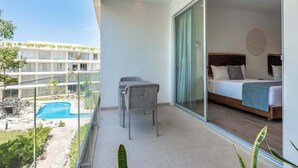 Un balcone con vista su una piscina, un letto con testiera in legno e un tavolo da pranzo con sedie.