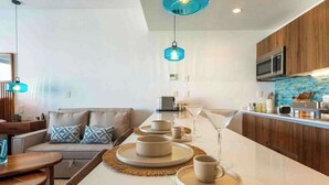 A modern kitchen with a central island, wooden cabinets, and blue pendant lights. - Playacar Studio | 4 Pools, Gym, AC & WiFi (Playa del Carmen)