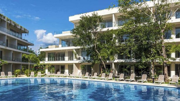 Un hotel moderno con piscina, lettini e un cielo azzurro limpido.