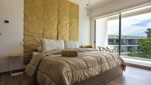 Una camera da letto moderna con un letto grande, una testiera in legno, un comodino e vista su un edificio attraverso un'ampia finestra.