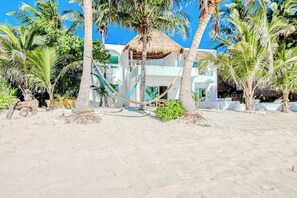 A beachside hotel with a thatched-roof structure, palm trees, and a hammock.