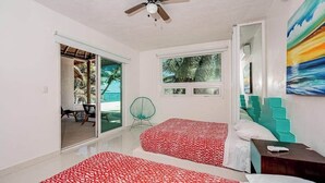 Un dormitorio con dos camas, un ventilador de techo, una ventana con vistas y una puerta que da a un área exterior.