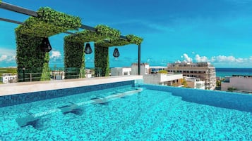 Una piscina infinita en la azotea con vistas despejadas al océano, rodeada de vegetación y arquitectura moderna.