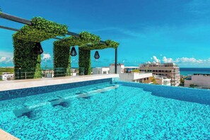 A rooftop infinity pool with a clear view of the ocean, surrounded by greenery and modern architecture. - Studio | Rooftop Pool & Gym, Steps to Beach (Playa del Carmen)