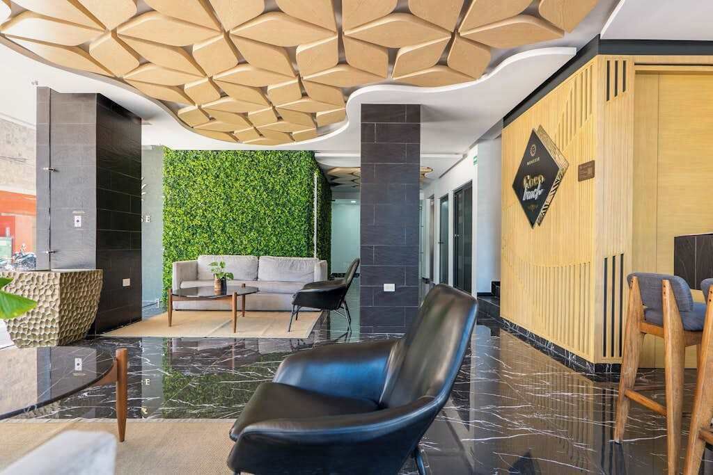 A modern lobby with a green wall, a reception desk, a sofa, and a black leather chair.