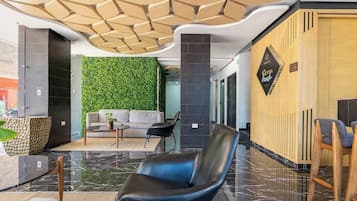 A modern lobby with a green wall, a reception desk, a sofa, and a black leather chair.