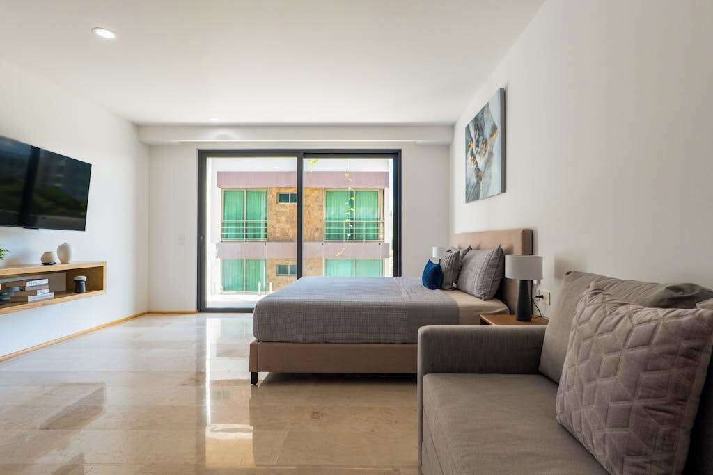 Un dormitorio moderno con cama, sofá, televisión y balcón con vistas a edificios.