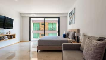 Un dormitorio moderno con cama, sofá, televisión y balcón con vistas a edificios.