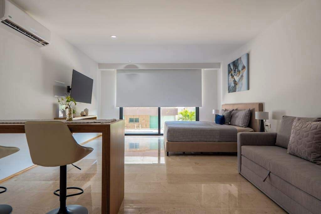 Una habitación de hotel moderna con cama, escritorio, silla, sofá, televisor y un gran ventanal.