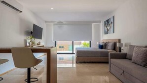 A modern hotel room with a bed, a desk, a chair, a sofa, a TV, and a large window. - Studio | Rooftop Pool & Gym, Steps to Beach (Playa del Carmen)