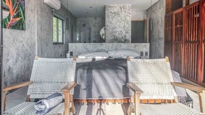 A bedroom with a bed, two wicker chairs, a large window, and a wooden door. - Beachfront 7BR Villa with Private Pool and Sauna (Tulum)