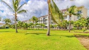 A hotel with a grassy courtyard, palm trees, and a multi-story building with balconies. - Mareazul Beachfront 2BR | Pool & Sea Views (Playa del Carmen)