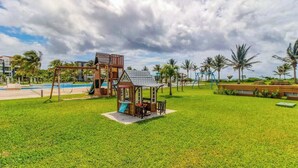A playground with a swing set, a slide, and a small shelter. - Mareazul Beachfront 2BR | Pool & Sea Views (Playa del Carmen)