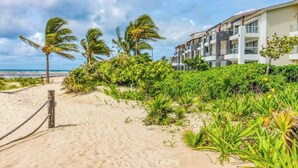A beachfront hotel with a sandy walkway, palm trees, and lush greenery. - Mareazul Beachfront 2BR | Pool & Sea Views (Playa del Carmen)
