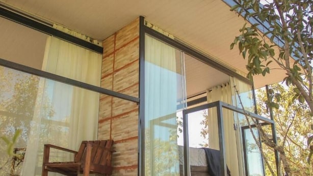 A modern building with large glass windows, a wooden chair, and a staircase leading to an upper level. - Chalés casa Borba  (Alto Paraíso de Goiás)