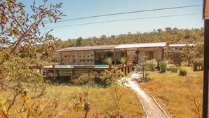 A rustic building with a corrugated metal roof, a wooden deck, and a gravel path leading to it. - Chalés casa Borba  (Alto Paraíso de Goiás)