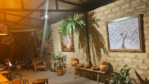 A rustic interior with a stone wall, wooden furniture, terracotta pots, and potted plants. - Chalés casa Borba  (Alto Paraíso de Goiás)