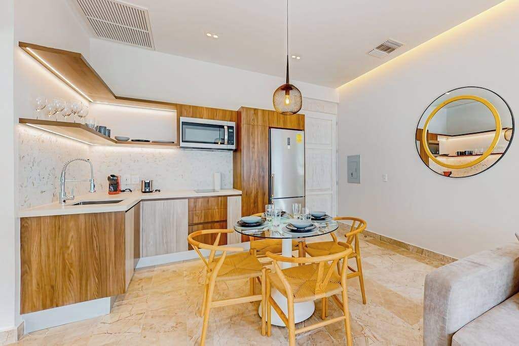 A modern kitchen with a dining area, wooden cabinets, a microwave, and a round mirror.