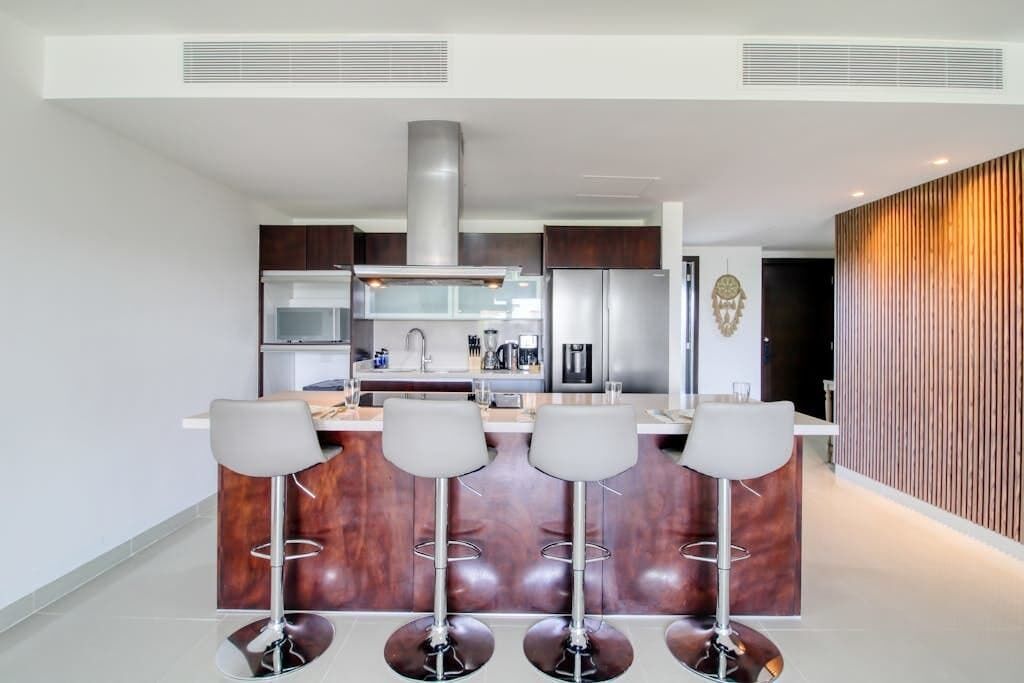 Een moderne keuken met een centraal eiland, roestvrijstalen apparatuur en een bar met krukken.