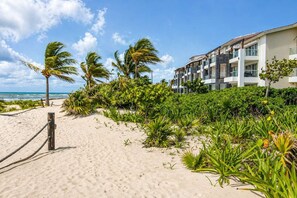 Ein Strandhotel mit einem Sandweg, Palmen und freiem Blick auf den Ozean.