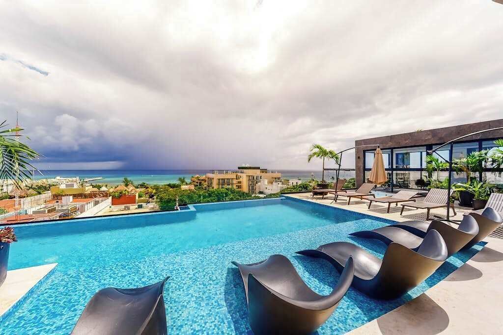 A pool with lounge chairs, a view of the ocean, and a building with large windows.