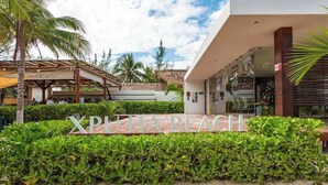 A sign for 'XPULAHABEACH' with a modern building and a covered area with palm trees. - Xpu-Ha Beachfront Villa 1: Private Pool & Gym (Playa del Carmen)