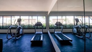 Ett gym med löpband och crosstrainers, stora fönster med utsikt över grönområden och byggnader, och ett blått golv.