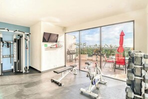 Een sportschool met trainingsapparatuur, een bank en uitzicht op het buitenlandschap door grote ramen.