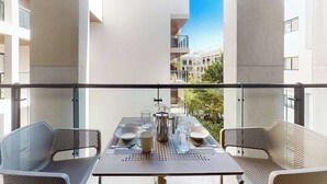 Un balcone con un tavolo apparecchiato per due, una sedia in metallo e vista su edifici limitrofi.
