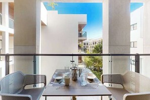 Ein Balkon mit Tisch für zwei Personen, einem Metallstuhl und Blick auf angrenzende Gebäude.