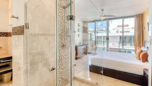 Ein modernes Hotelzimmer mit Duschkabine aus Glas, einem Bett mit Blick und einem Balkon mit Stadtansicht.