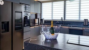 Eine moderne Küche mit Marmorarbeitsplatte, einem Weinkühlschrank mit Gläsern und einem großen Fenster mit Jalousien.