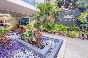 En modern hotellentrén med en vacker trädgård, en skylt med texten ”SIAAN” och en utsikt över hotellets interiör.