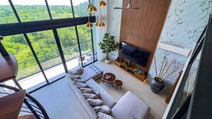 Ein modernes Wohnzimmer mit großem Fenster, einer Couch, einem Fernseher und einer Pflanze.