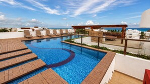 Piscina no terraço com deck de madeira, espreguiçadeiras e vista para o oceano.