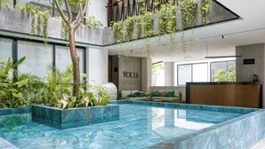 A modern indoor pool area with a reception desk, seating area, and greenery. - Bright Condo: Rooftop Ocean Pool, Walk to Beach (Playa del Carmen)