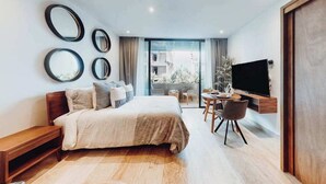 A modern bedroom with a bed, bedside tables, a TV, a balcony with a view, and a dining area. - Bright Condo: Rooftop Ocean Pool, Walk to Beach (Playa del Carmen)