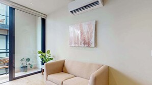 A modern living room with a beige sofa, a large window, and a potted plant. - Modern 1BR Condo | Rooftop Pool & Gym, Near Beach (Playa del Carmen)