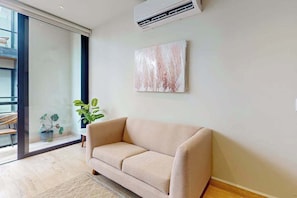 A modern living room with a beige sofa, a large window, and a potted plant. - Modern 1BR Condo | Rooftop Pool & Gym, Near Beach (Playa del Carmen)